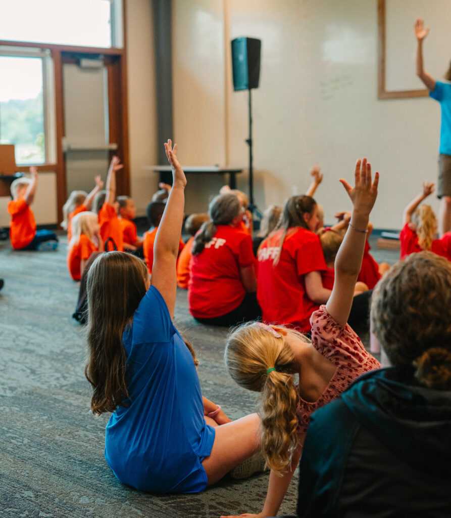 A group of kids raising their hands in a classroom. 