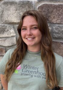Woman wearing a green shirt standing outside against a brick wall smiling. 