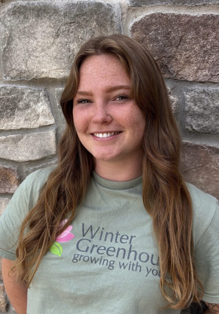 Woman wearing a green shirt standing outside against a brick wall smiling.